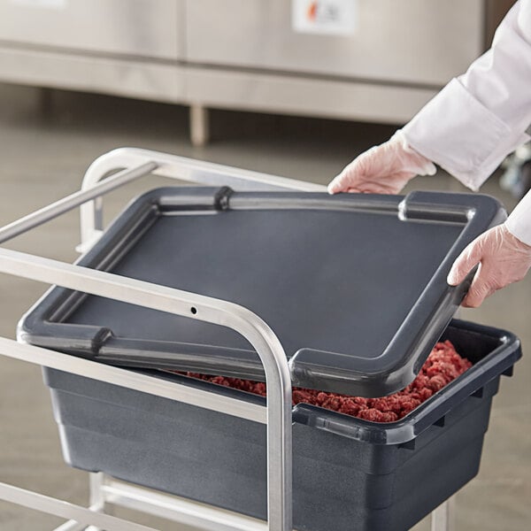 A person wearing gloves placing a tray of meat in a dark gray plastic tote with a recessed lid.