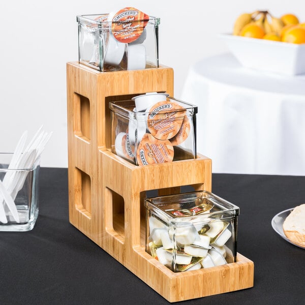 A Cal-Mil bamboo three tier jar display on a table with jars of tea and coffee.