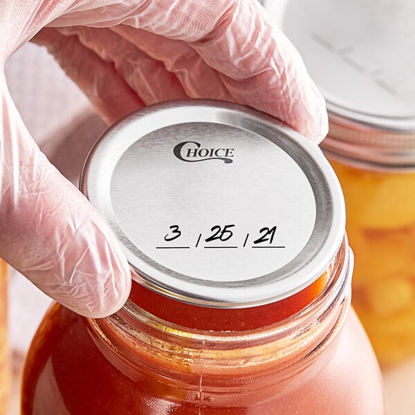 A person in gloves holding a Regular Mouth canning jar with a label of red sauce.