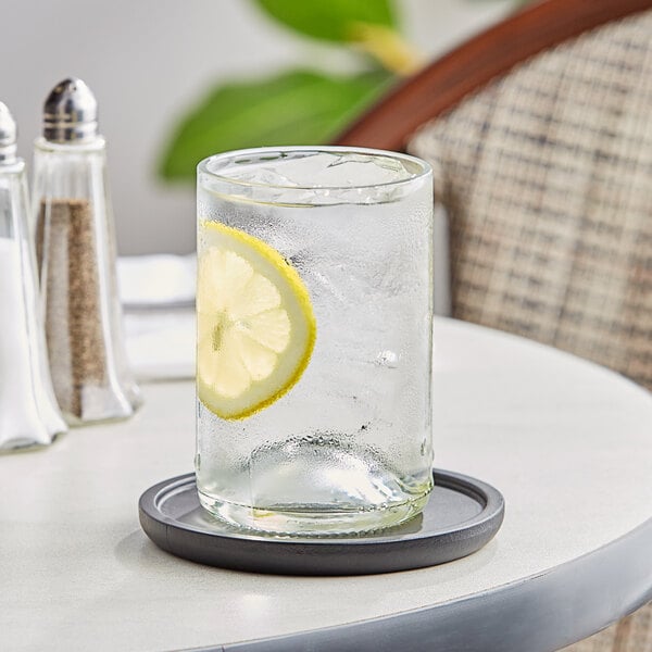 A Fortessa clear wine tumbler with a lemon slice in a glass of water on a coaster.