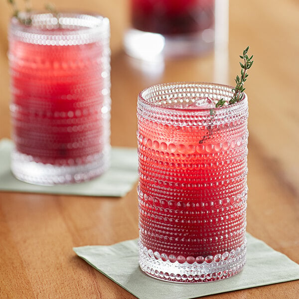 Two Fortessa Jupiter clear beverage glasses filled with red drinks on a table.