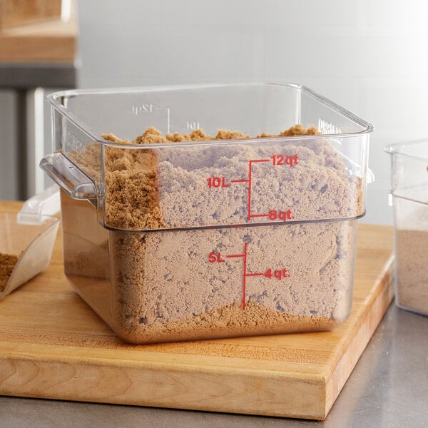 A Cambro clear polycarbonate food storage container filled with brown powder on a kitchen counter.