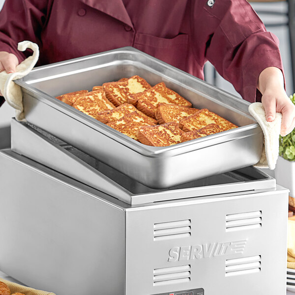 A woman using a Choice stainless steel angled display adapter to serve food in a metal pan.