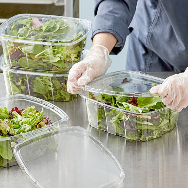 A person in gloves putting lettuce and greens in a clear plastic container.