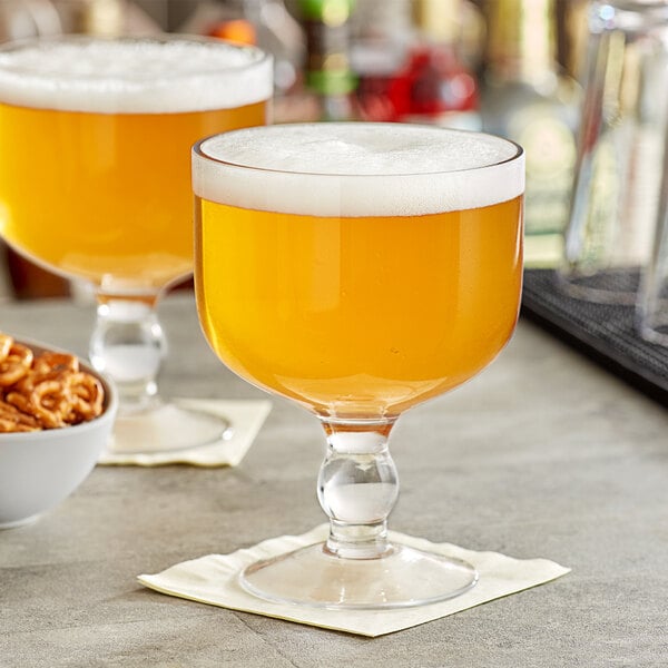 Two Acopa giant schooner glasses of beer on a table with a bowl of pretzels.