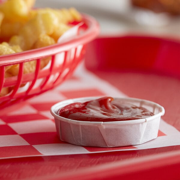 A red basket of french fries with a bowl of ketchup on a table.