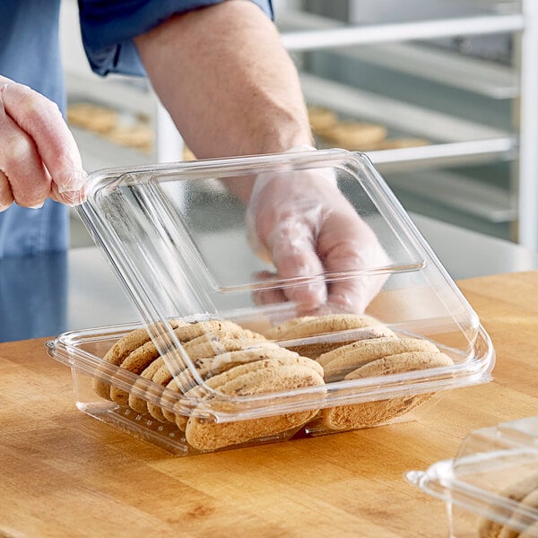 A person in gloves holding a Clear PET Bakery Container of cookies.