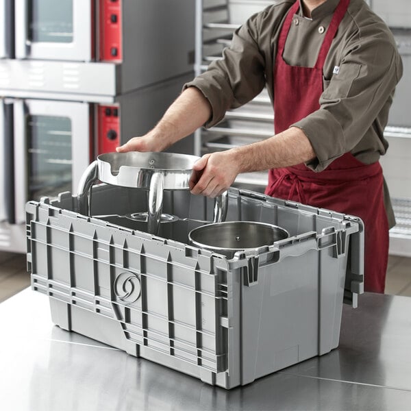 A man in a red apron holding a Choice stackable grey chafer tote/storage box with attached lid.