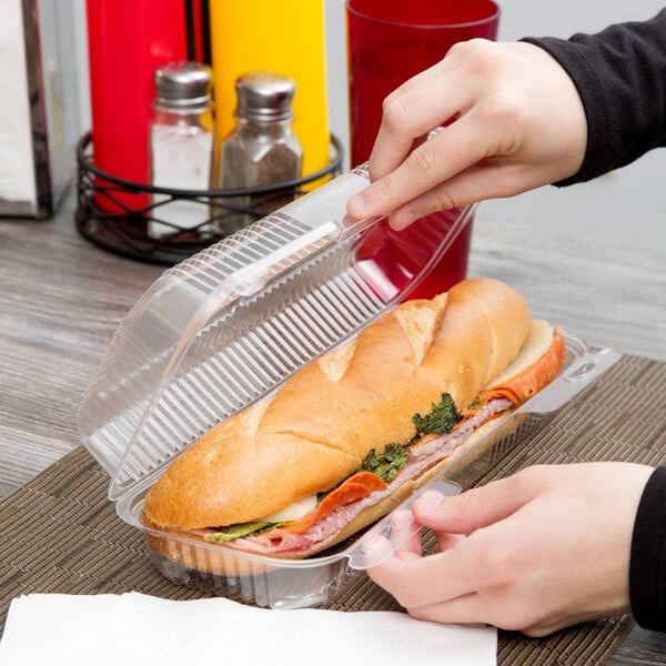 A person putting a sandwich in a Duralock clear hinged lid plastic container.