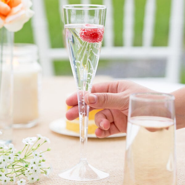 A hand holding a WNA Comet clear plastic champagne glass full of liquid.