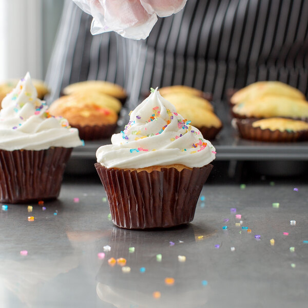 A cupcake with white frosting and small colored sprinkles in a mini glassine baking cup.
