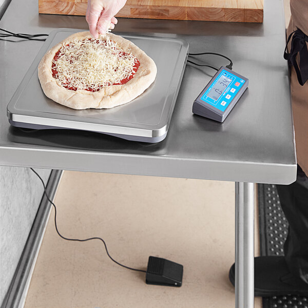 A person using an AvaWeigh pizza scale to weigh a pizza on a white counter.