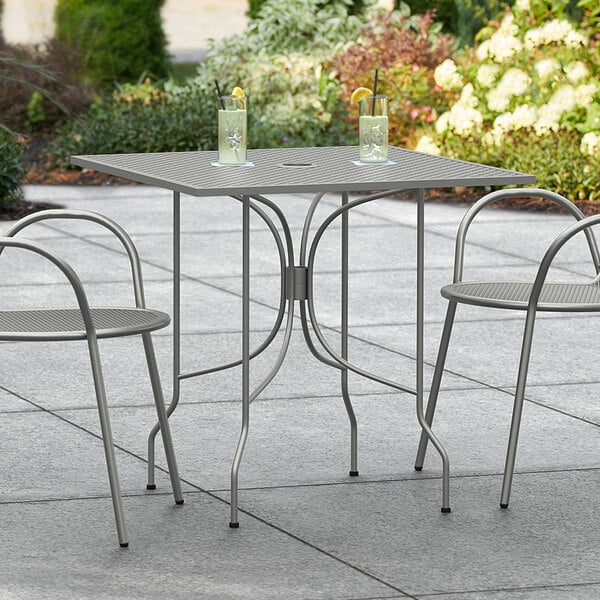 A Lancaster Table & Seating Harbor Gray metal table with ornate legs on a patio.