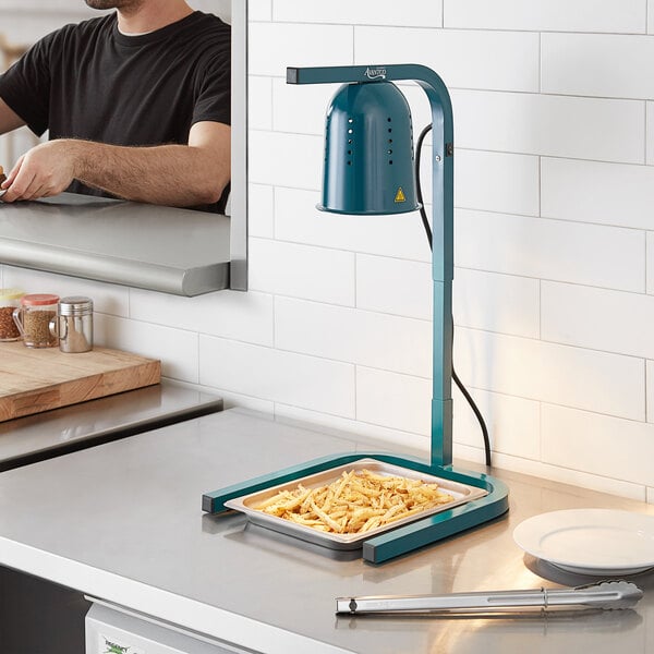 A man using an Avantco green free standing heat lamp to cook food on a countertop in a professional kitchen.