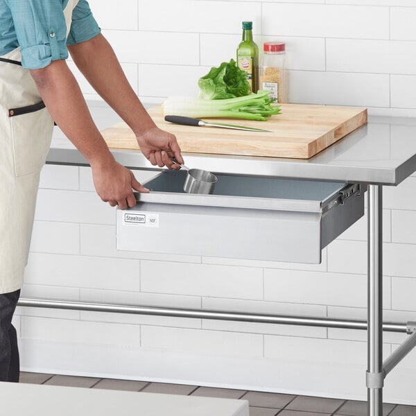 A man in an apron using a Steelton stainless steel drawer in a professional kitchen.