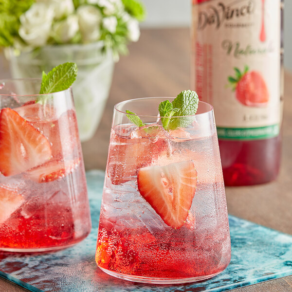 Two glasses of red DaVinci Gourmet strawberry drinks with strawberries and mint leaves.