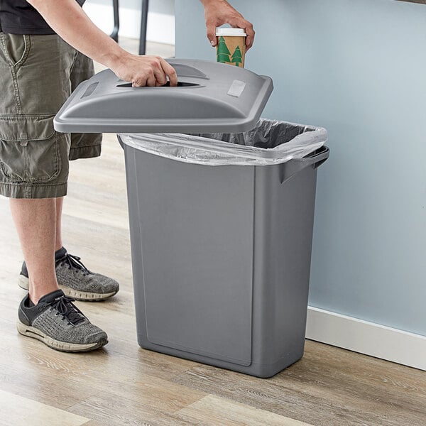 A hand opening a Lavex Slim Rectangular trash can to put a coffee cup inside.