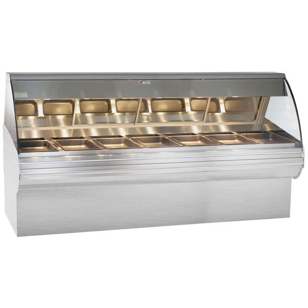 An Alto-Shaam stainless steel heated display case with curved glass and trays of food.