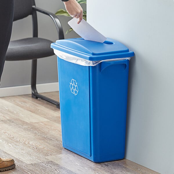 A woman putting paper into a Lavex blue recycle bin with a paper slot lid.