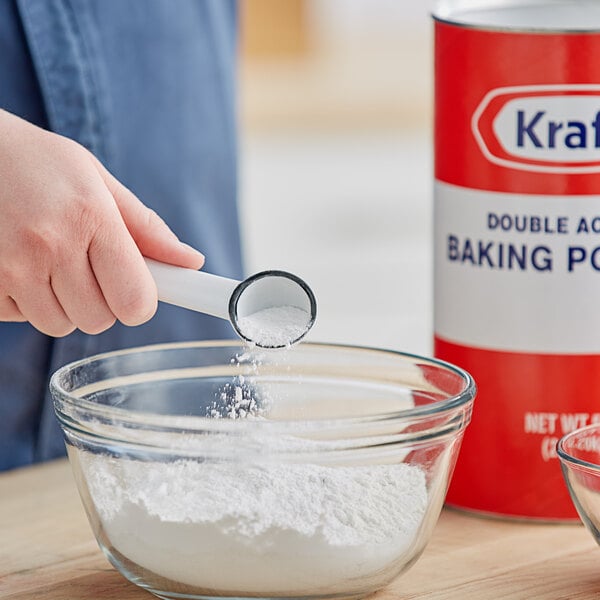 A hand pouring Kraft baking powder into a bowl.