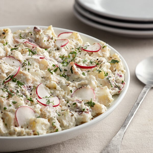 A bowl of potato salad with radishes and parsley next to a pail of Kraft Miracle Whip.