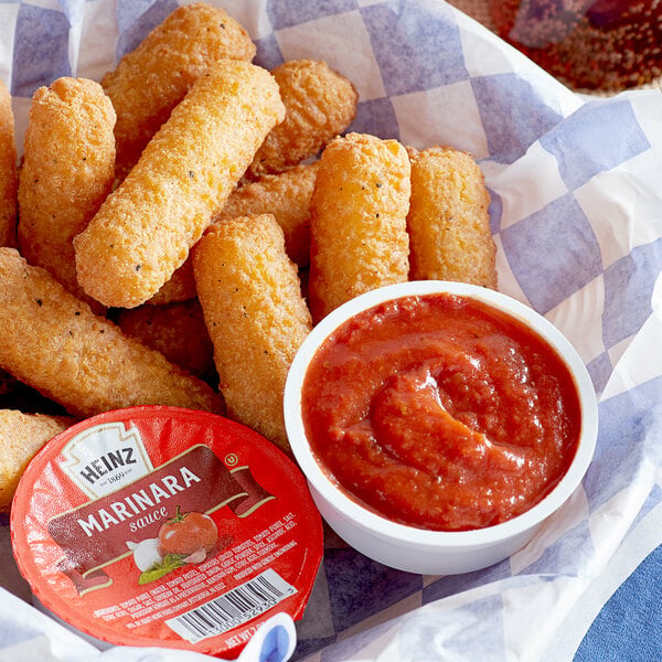 Fried food in a basket with a bowl of Heinz marinara sauce.