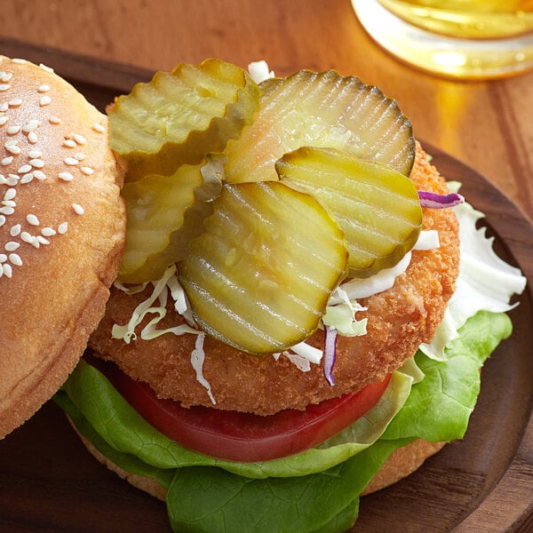 A burger with Heinz dill pickle slices on a wooden plate.