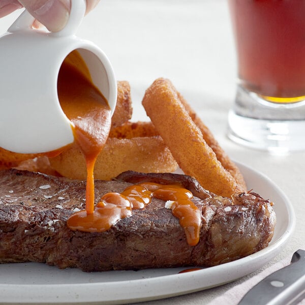 A hand pouring Heinz 57 sauce onto a steak on a plate.