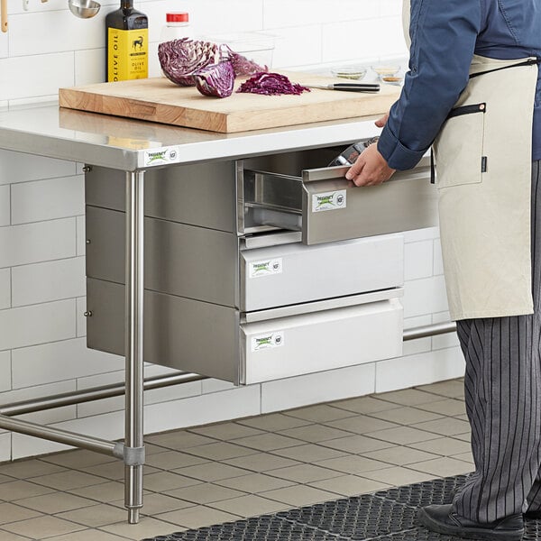 A man in a white apron opening a Regency stainless steel drawer in a kitchen.