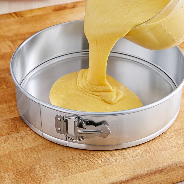 A person pouring yellow batter into a Choice natural finish aluminum springform cake pan.