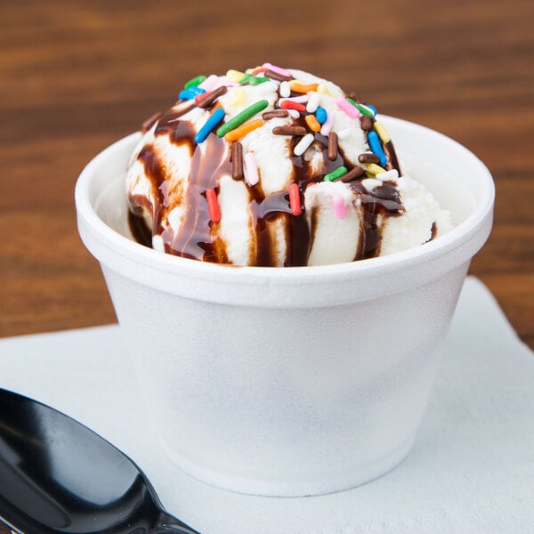 A Dart white foam food container filled with ice cream, chocolate syrup, and sprinkles.