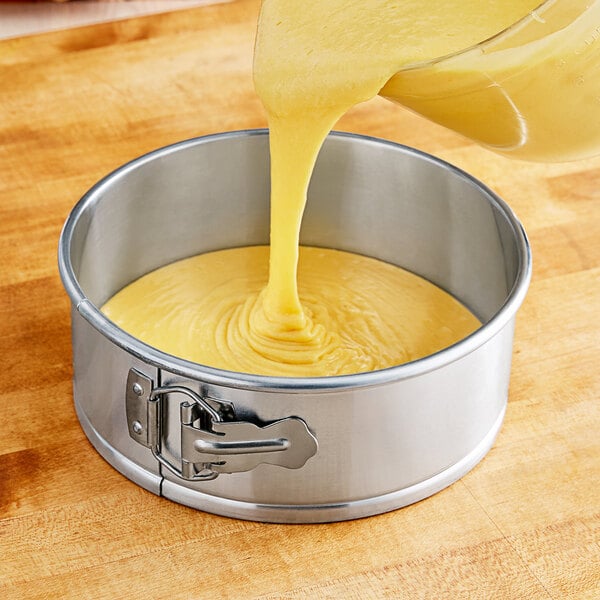 A bowl of yellow cake batter being poured into a Choice springform cake pan.