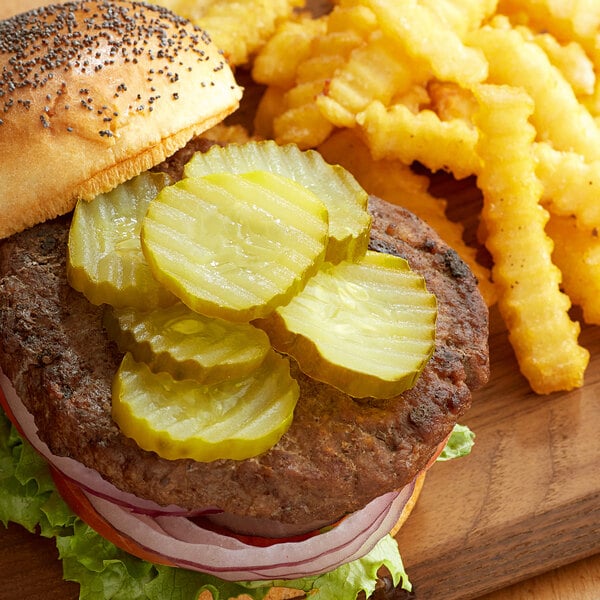 A hamburger with Heinz Dill Pickles on top and fries on a wooden board.