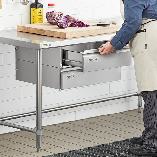 A man in an apron is standing next to a metal counter with Regency stainless steel double-stacked drawers on top.
