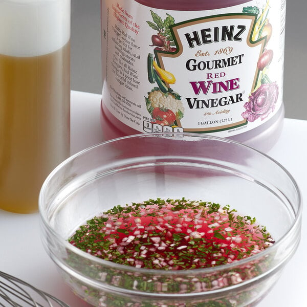 A bowl of red sauce with herbs and a bottle of Heinz red wine vinegar on a kitchen counter.