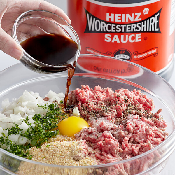 A hand pouring Heinz Worcestershire sauce into a bowl of ground meat.