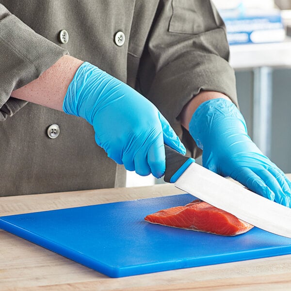A person in blue Noble gloves cutting a piece of salmon on a cutting board.