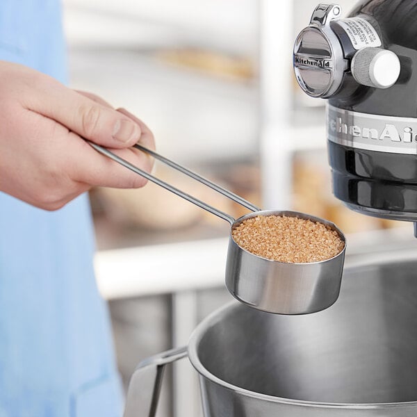 A person using an American Metalcraft stainless steel measuring cup to pour sugar.