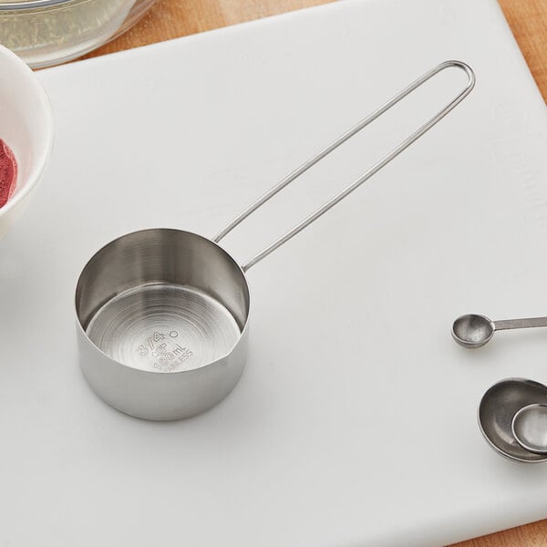An American Metalcraft stainless steel measuring cup with wire handle on a cutting board.