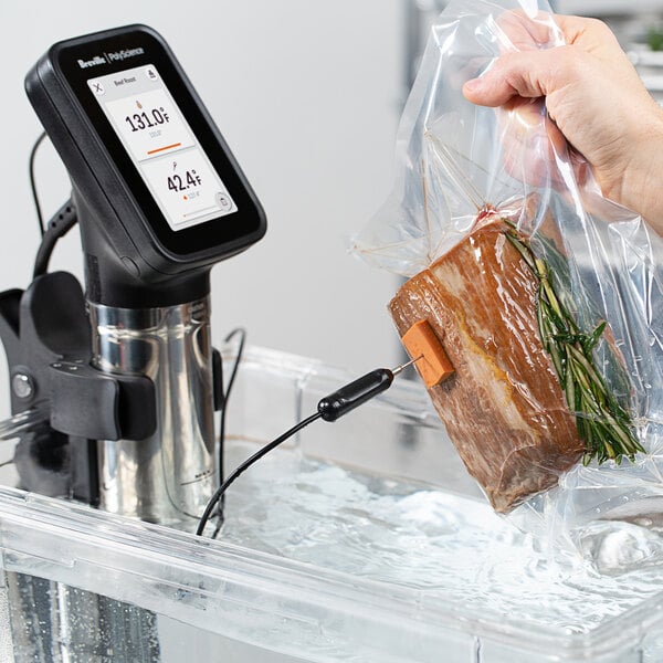 A hand using a Breville HydroPro Plus to cook meat in a plastic bag.