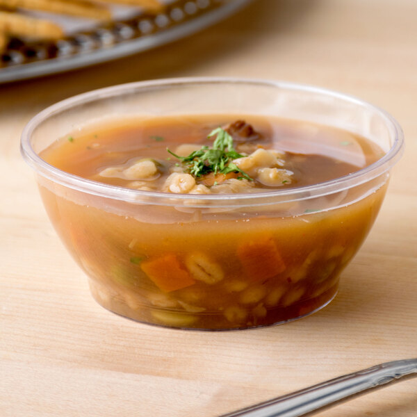 A clear Fineline plastic bowl filled with soup with a spoon.