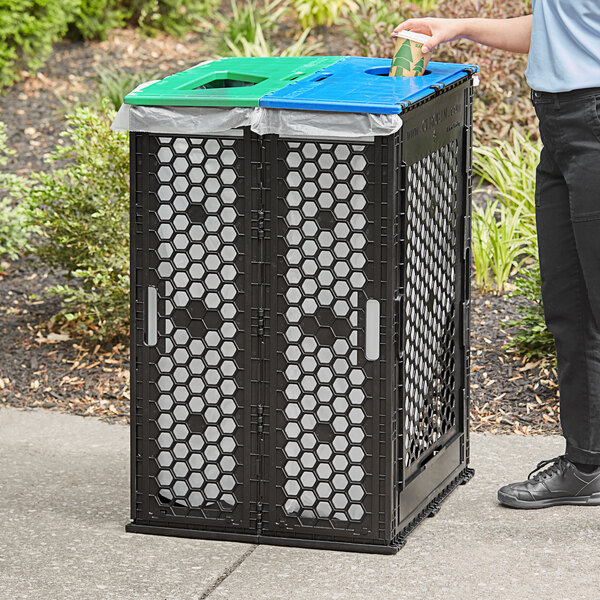 A woman standing next to a black Cerobin dual-stream recycling/compost receptacle with a blue lid.