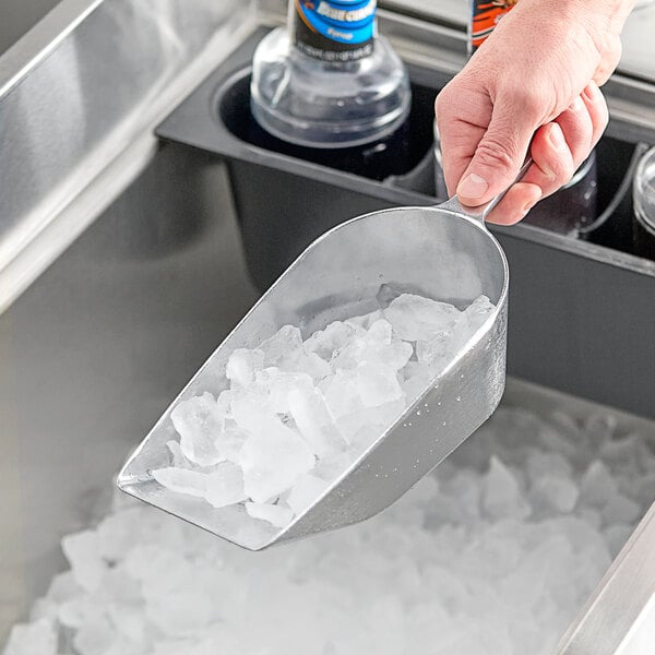 A hand holding a Choice flat bottom aluminum scoop full of ice.
