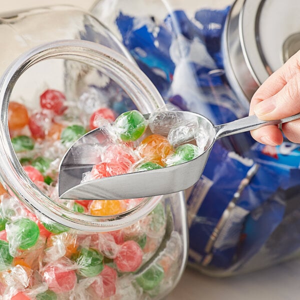 A hand using a Choice aluminum scoop to get candy from a jar.