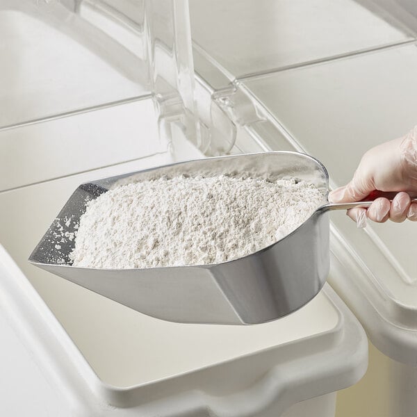 A person using a Choice aluminum flat bottom scoop to scoop flour.