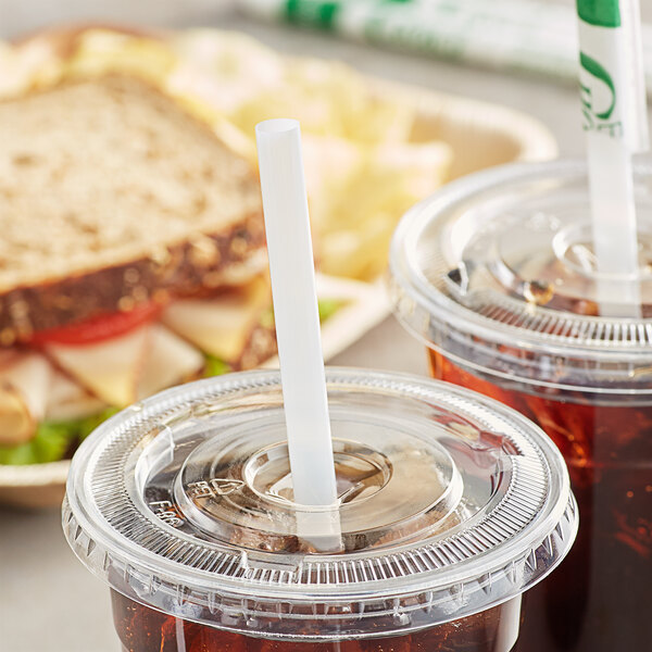 A white plastic container with a sandwich and drink, with a plastic lid and straw inside.