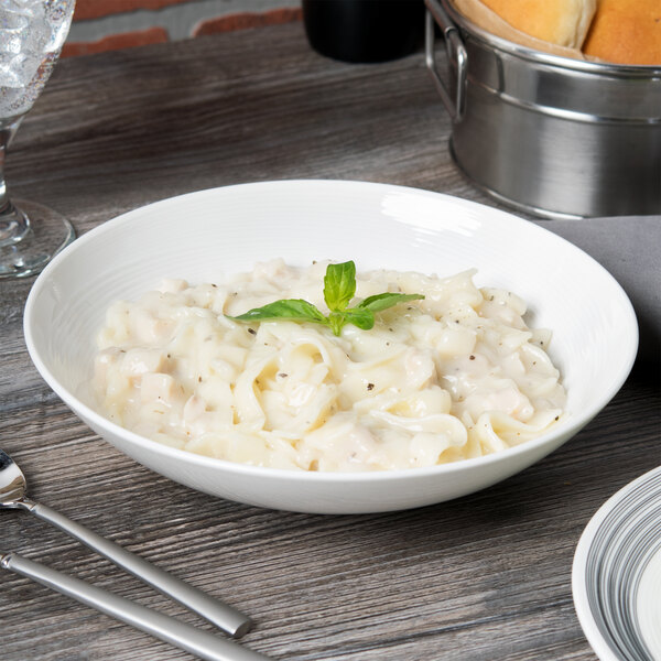 A Reserve by Libbey white porcelain coupe bowl filled with pasta with a spoon and fork on the table.
