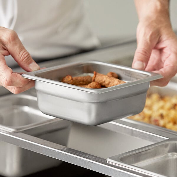 A person holding a Choice stainless steel steam table pan full of food.