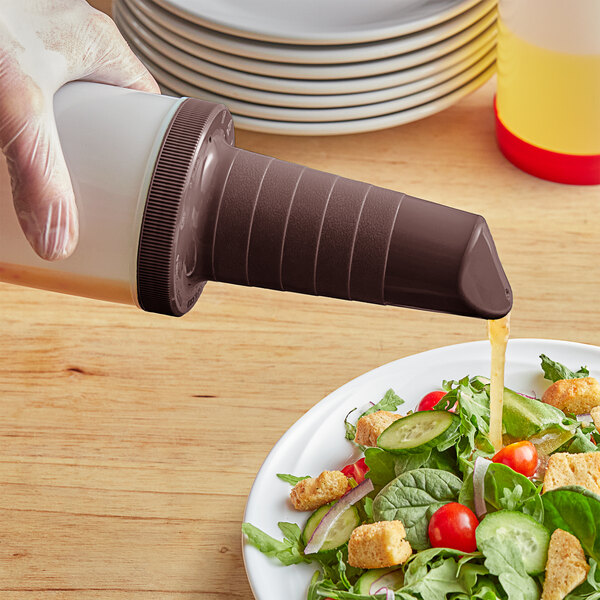 A hand using a Tablecraft brown plastic pour spout to pour dressing on a salad.