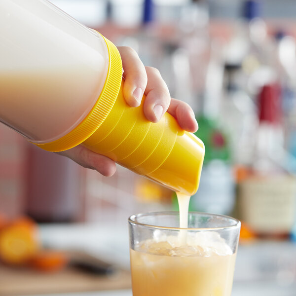 A hand using a Tablecraft yellow pour spout to pour a drink into a glass.